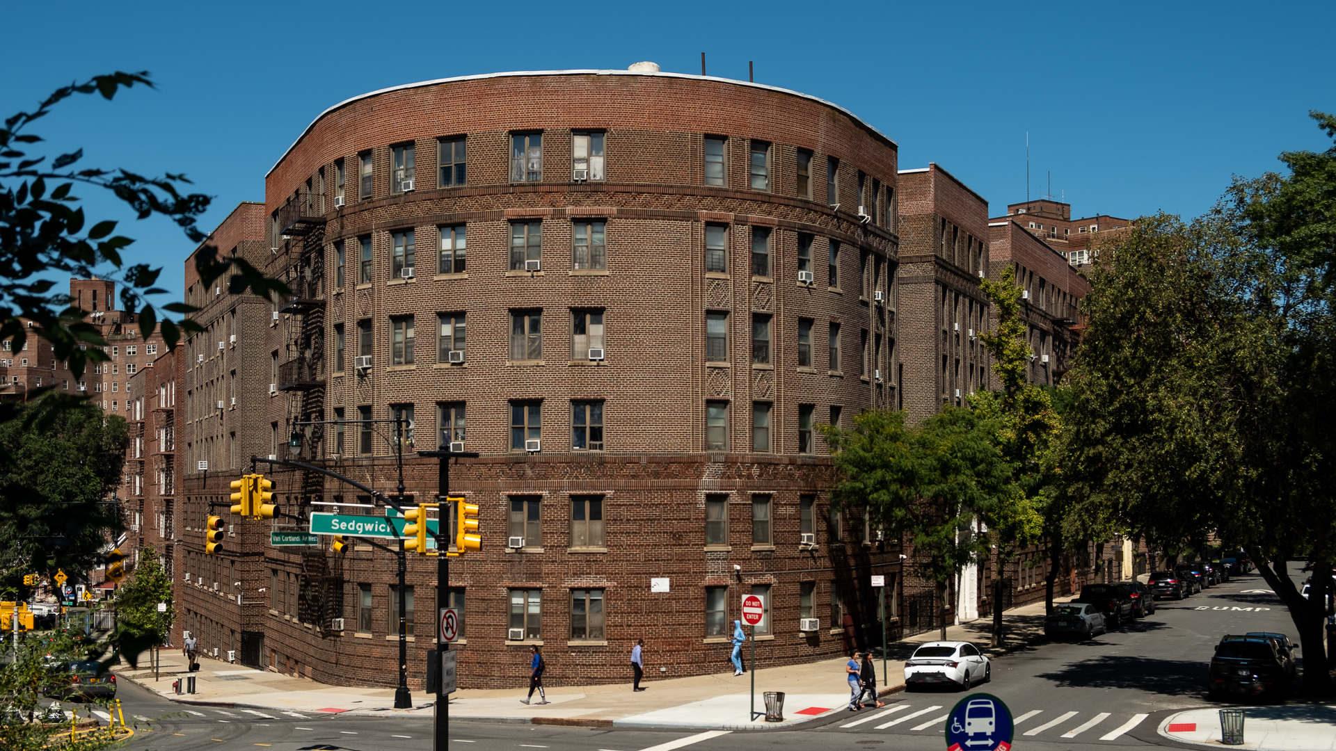 Photograph of a large curved pre-war brick rent-stabilized apartment building on the corner of Sedgwick Avenue in the Bronx under a clear blue sky